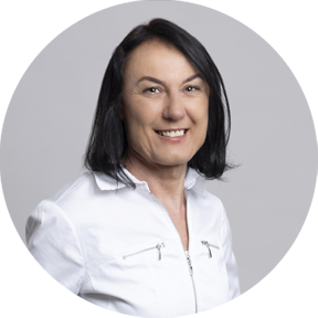 Frau mit schwarzen, schulterlangen Haaren, weißer Jacke und schwarzer Hose, lächelt in die Kamera