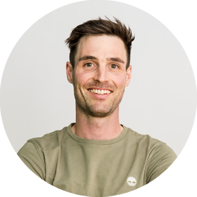 Junger Mann mit kurz geschnittenen Haaren, grünem T-Shirt und verschränkten Armen, lächelt in die Kamera